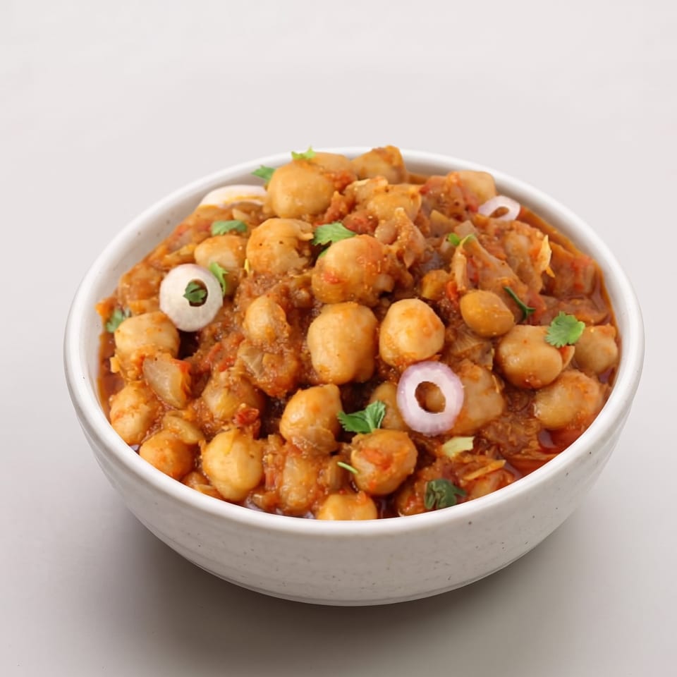Bowl of chickpea curry garnished with cilantro and sliced red onion.
