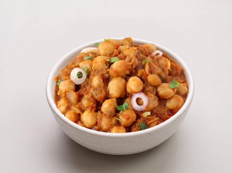 A white bowl filled with chana masala, garnished with red onion rings and cilantro.